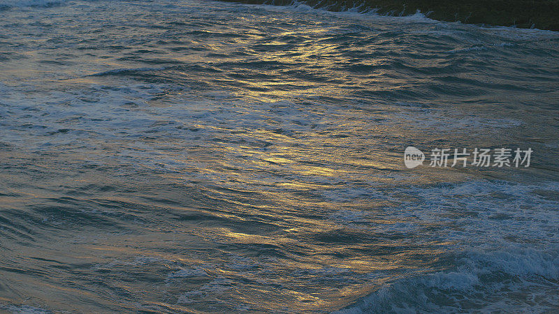 黑色海面上的波浪特写，金色的夕阳反射在水面上