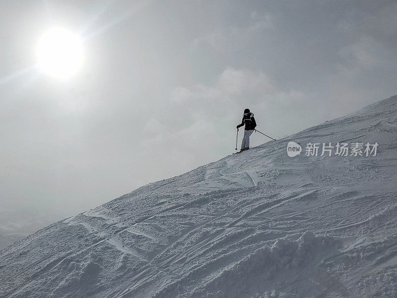 成熟女子滑雪者在天际线山脊与低清晨太阳在她身后。