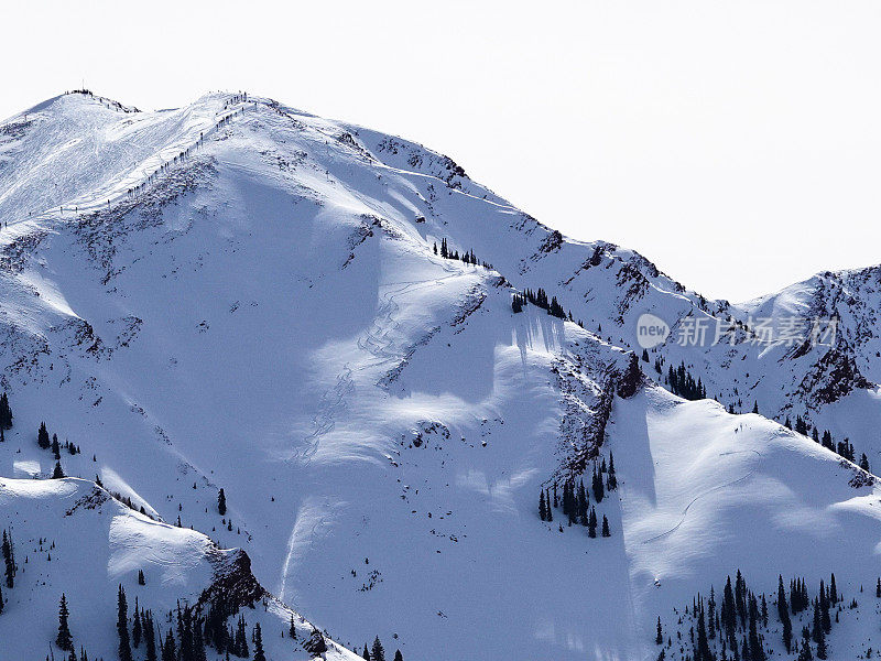 长焦视图数十名滑雪者和滑雪板徒步到12392英尺的高地峰滑雪碗。