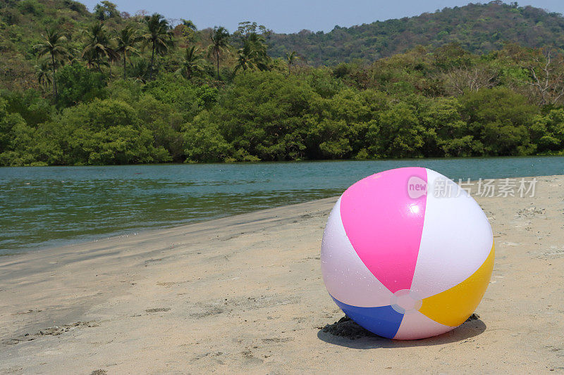 在泻湖沙滩上的沙滩球的特写图像，塑料，色彩鲜艳的儿童沙滩玩具，海洋和林地背景，重点在前景