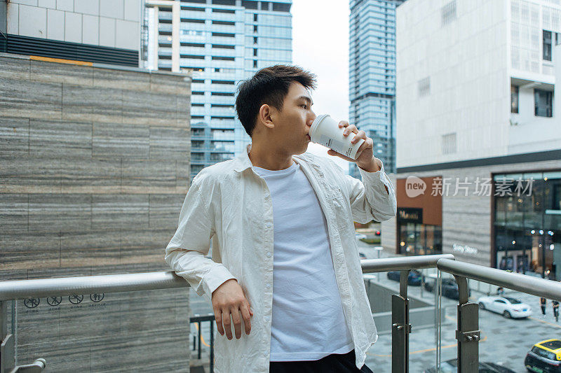 一个阴天，一位男商人正在公司外的阳台上休息咖啡休息——下班后喝一杯咖啡，促进健康，工作生活平衡