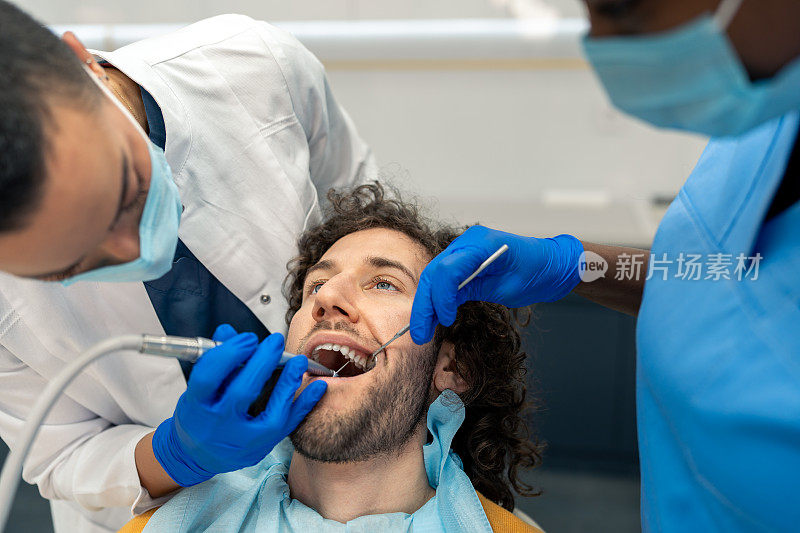 女牙医与牙医助理用牙钻在病人的牙齿上工作