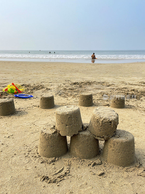 退潮时沙滩上用塑料桶和铁锹堆成的沙堡，塑料沙滩袋，退潮背景下的大海，重点在前景