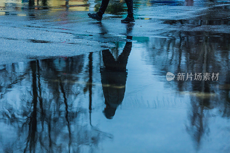 柏油路上的水坑。多雨的天气。下雨了。人的轮廓