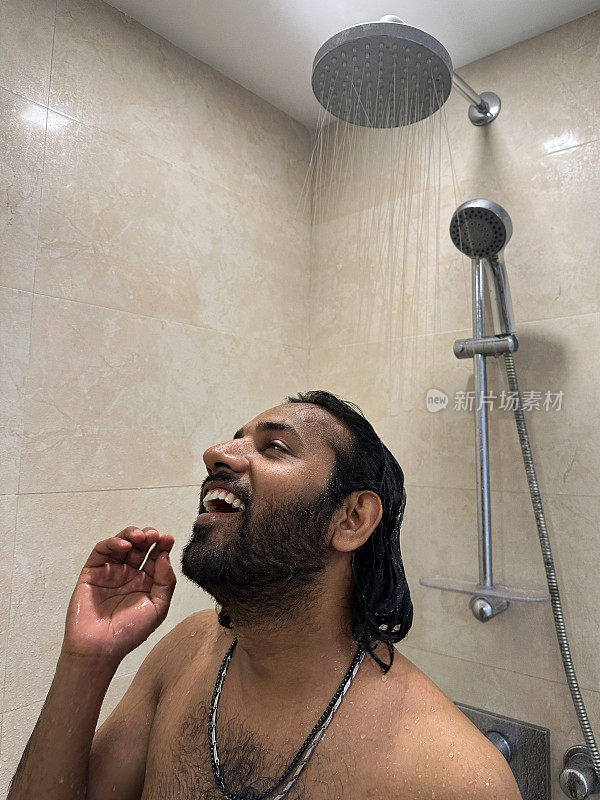 印度男子在淋浴间洗头的特写照片，洗发水泡沫在流水下冲洗掉，抬头看，棕色马赛克瓷砖的墙壁，重点在前景