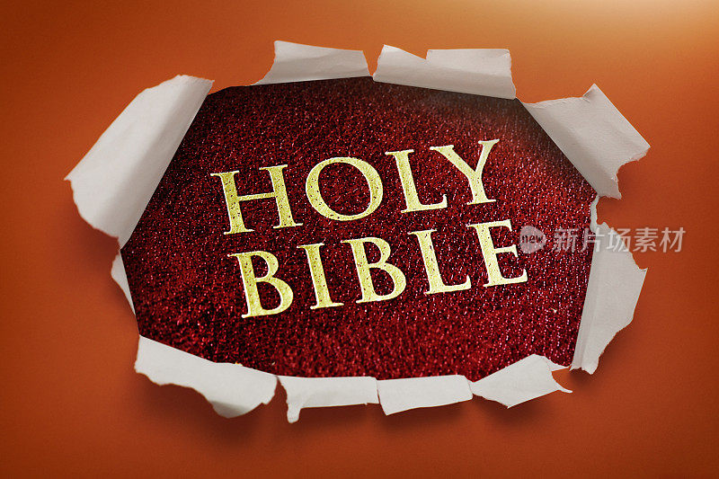 圣经的封面和标题透过撕开的锯齿边缘的纸洞露出来，背景是深橙色