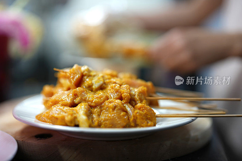 一个女人在厨房里准备沙茶，用竹签串生肉的特写镜头