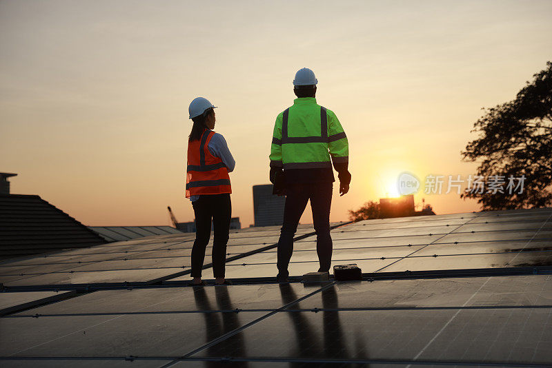 剪影网站太阳能服务工程师团队在太阳能屋顶上对着夕阳工作
