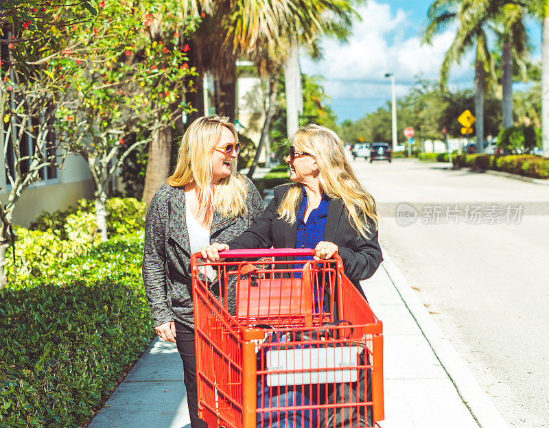 两个快乐的女人一起购物，在一家零售店外推着购物车