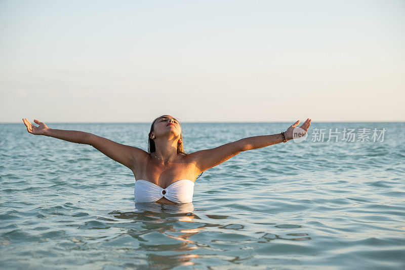 美丽的年轻女子在海边微笑，在平静的海面上欣赏日落和海浪