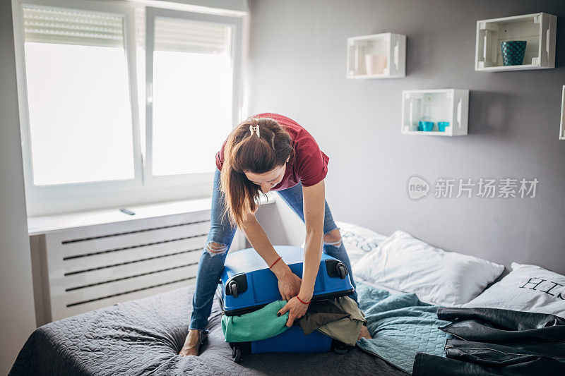 年轻女子试图合上满满的行李箱