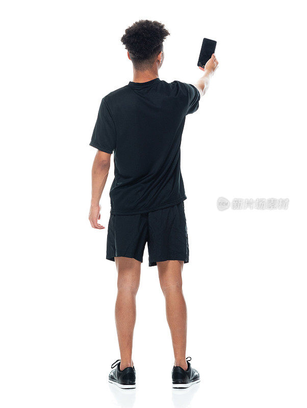 非裔美籍男性穿着运动鞋和使用手机站在白色背景前拍照