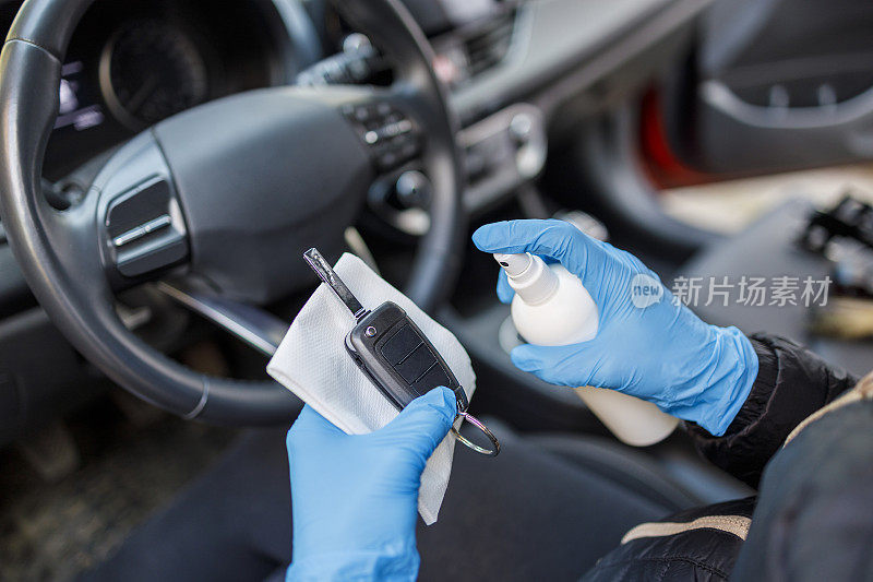 戴防护橡胶手套的人把车钥匙放在纸巾上，然后喷洒消毒剂