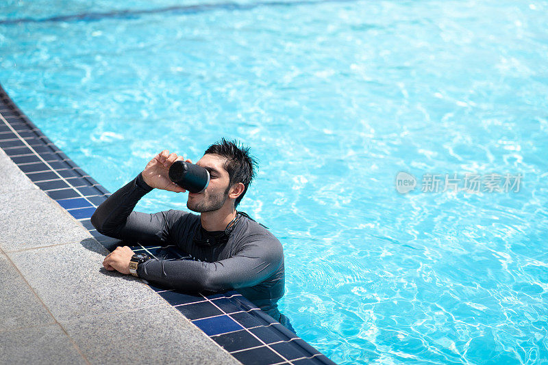 一个健康的男人在一个阳光明媚的夏天在游泳池边喝酒