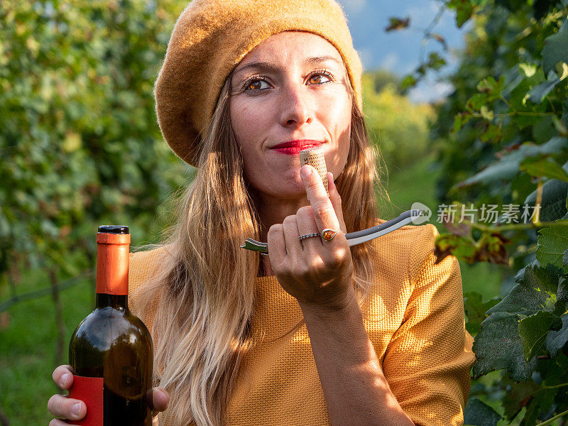 年轻女子在秋天的葡萄园里闻软木塞红葡萄酒的香气