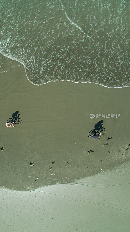 上下无人机拍摄的海浪接近骑在海滩上的自行车