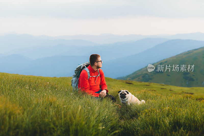 一个年轻的背包客和他的狗在山中享受日落，感受自由和幸福