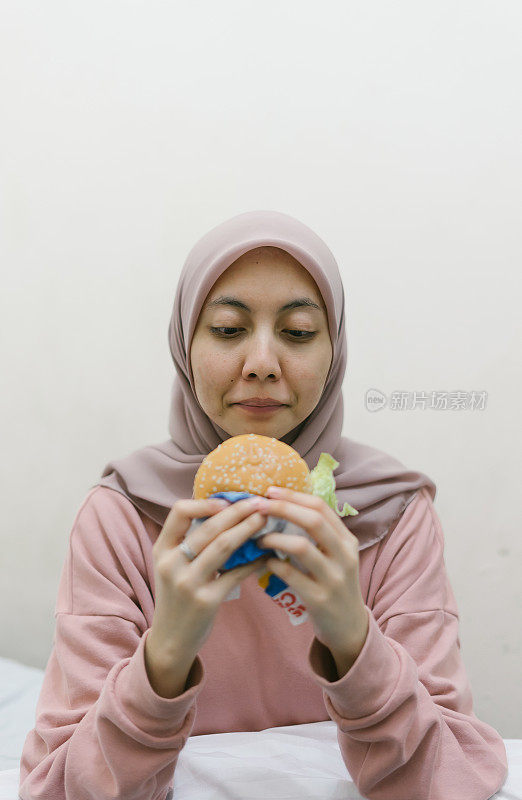 年轻的千禧一代亚洲女性在卧室里吃汉堡