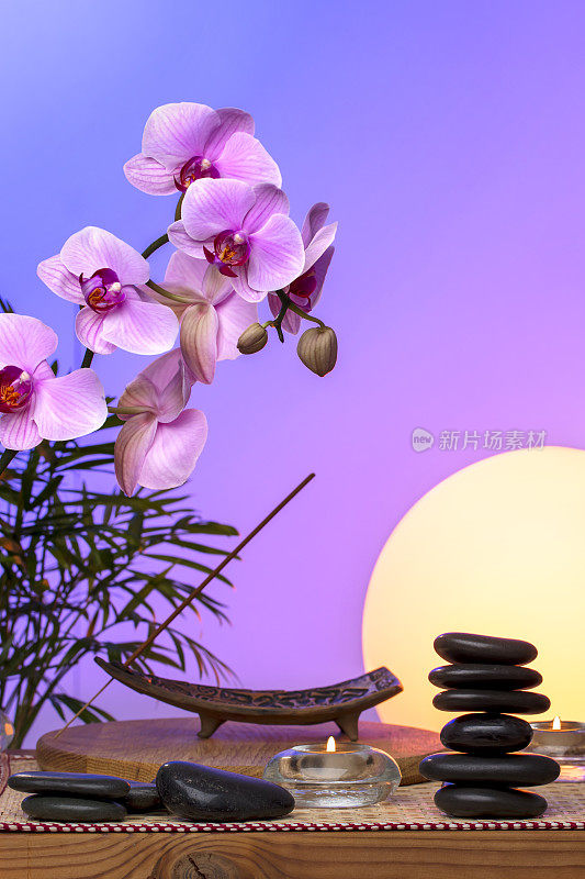 禅宗概念-兰花花，黑色按摩石，竹植物，蜡烛在一个木制桌子日落