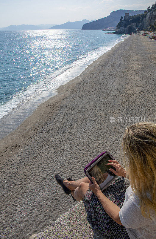 在海岸线上的石墙上，一个女人在使用数字平板电脑