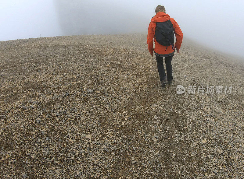 年轻的女登山运动员在雾中爬下一座山