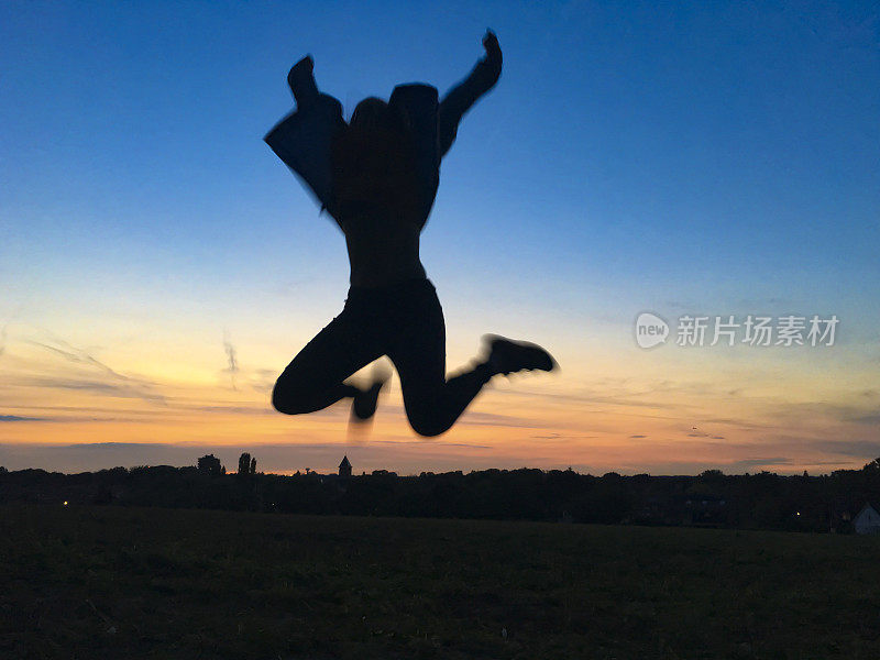 少女的剪影在空中跳跃的夕阳背景