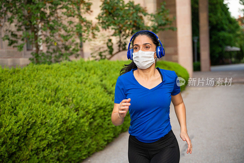 想在流感大流行期间增强免疫力的年轻女性，可戴防护口罩和耳机在户外跑步