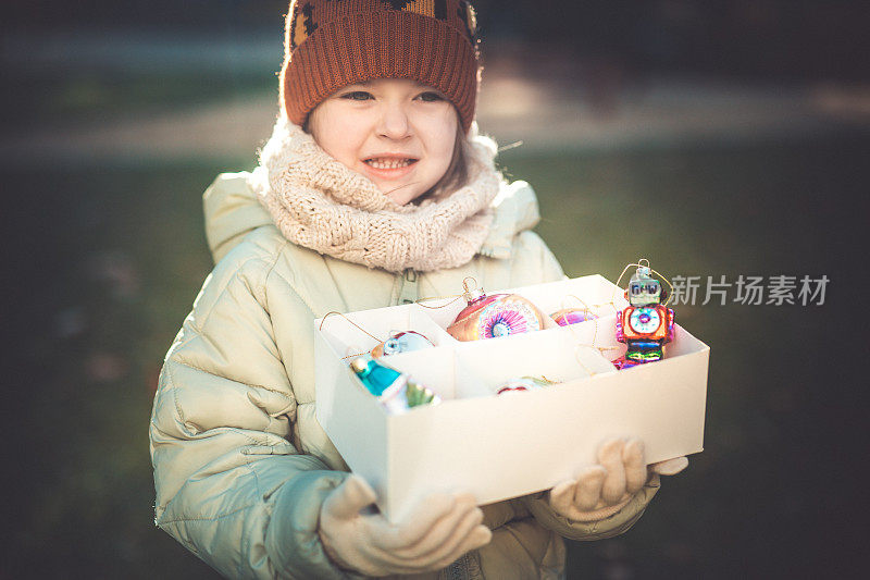 一个学龄前的小女孩手里拿着盒子里的圣诞装饰品