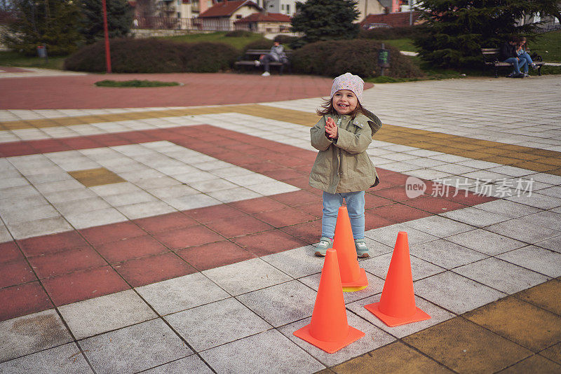 可爱的蹒跚学步的女孩有这么多的乐趣，而玩橙色的锥形
