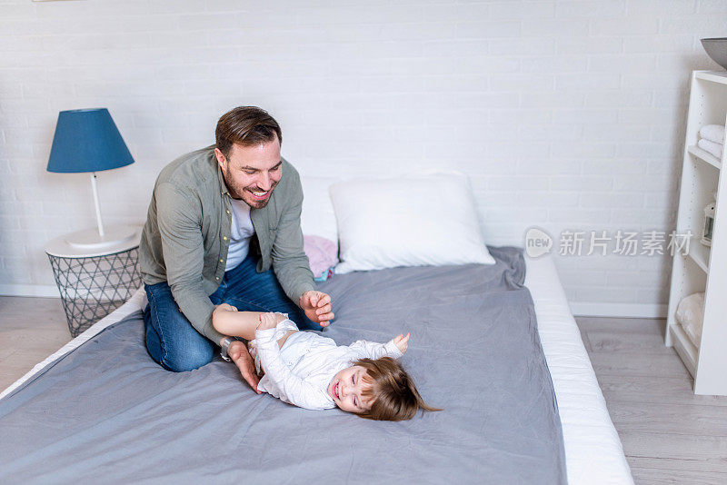 微笑的年轻父亲在给小女儿换尿布的时候和她玩得很开心