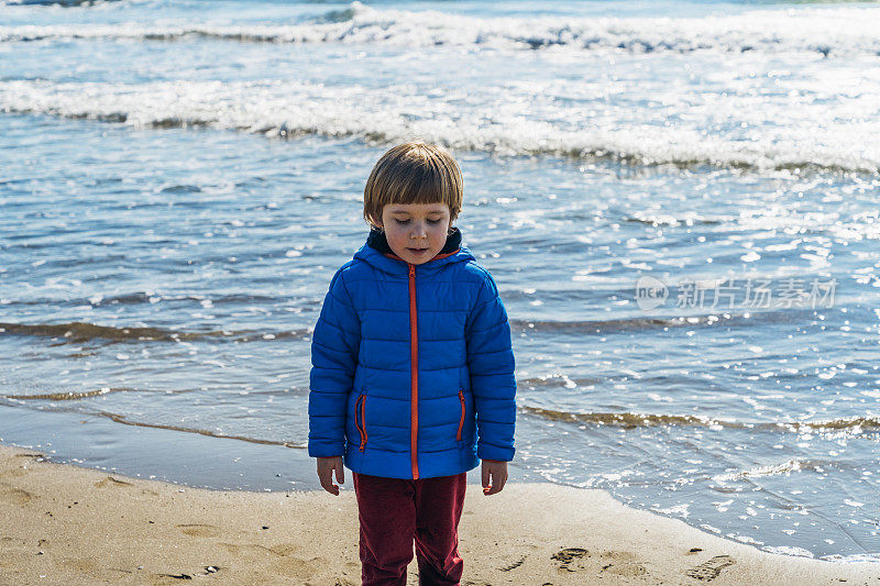一个可爱的蹒跚学步的小孩在冬天的海滩上玩耍