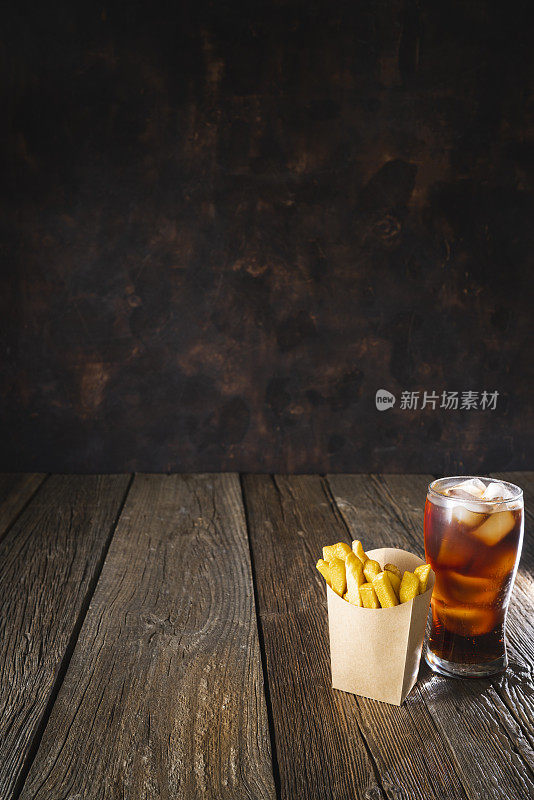 深色木桌上放着牛皮纸盒子装的可乐苏打杯和一次性薯条