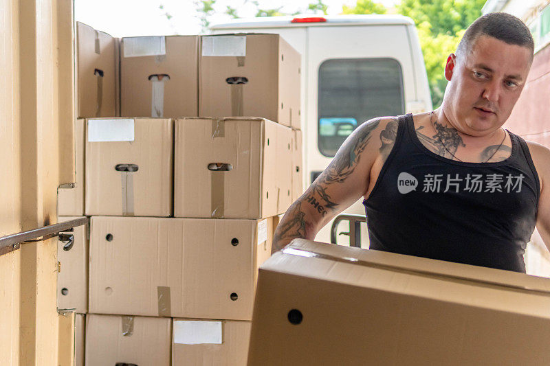 勤劳的纹身手工工人在仓库搬运非常重的大箱子准备出口