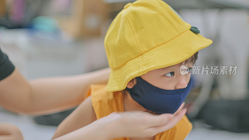 一位亚洲华人母亲在出门前帮助她的儿子戴上防护口罩和帽子