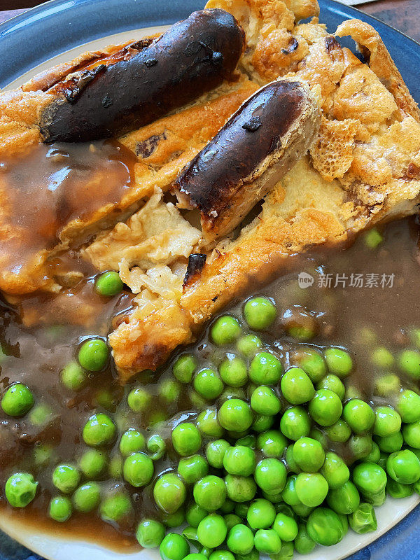 全框图像自制的传统英国蟾蜍在洞食谱与多汁的猪肉香肠，约克郡布丁面糊和焦糖洋葱，青豆和肉汁在白色盘子与蓝色边缘，提高视野