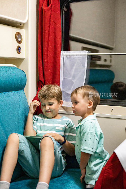 两个热情的小男孩在舒适的沙发上用平板电脑上网乘火车旅行
