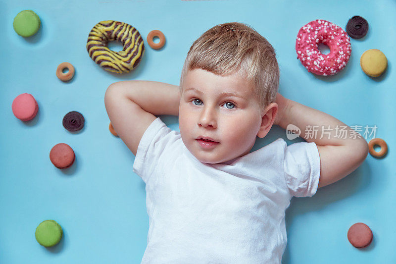 可爱的微笑的孩子甜甜圈和法国马卡龙在蓝色的背景。模拟白色t恤。国家甜甜圈日概念。快乐的童年概念