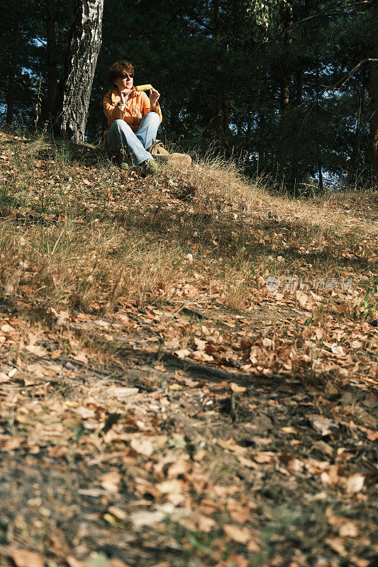 开朗成熟的女人在秋天的自然公园休息时享受烤玉米