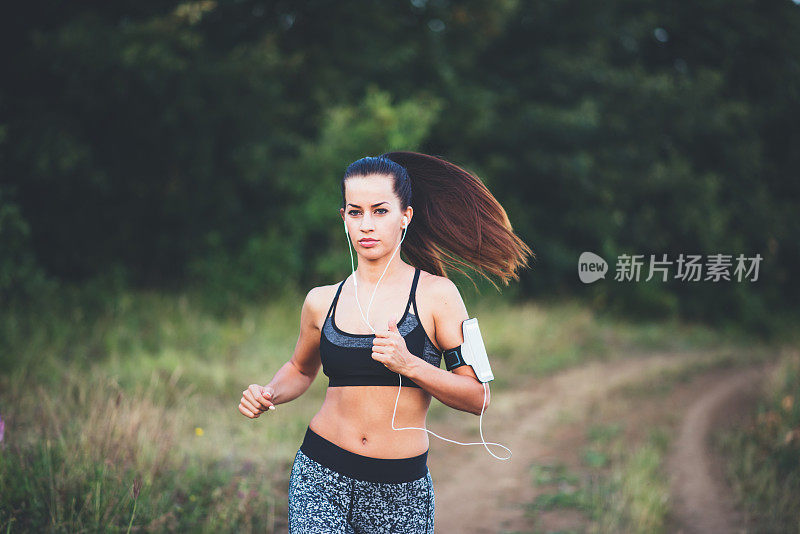 年轻的运动女孩奔跑在农村的道路在日落