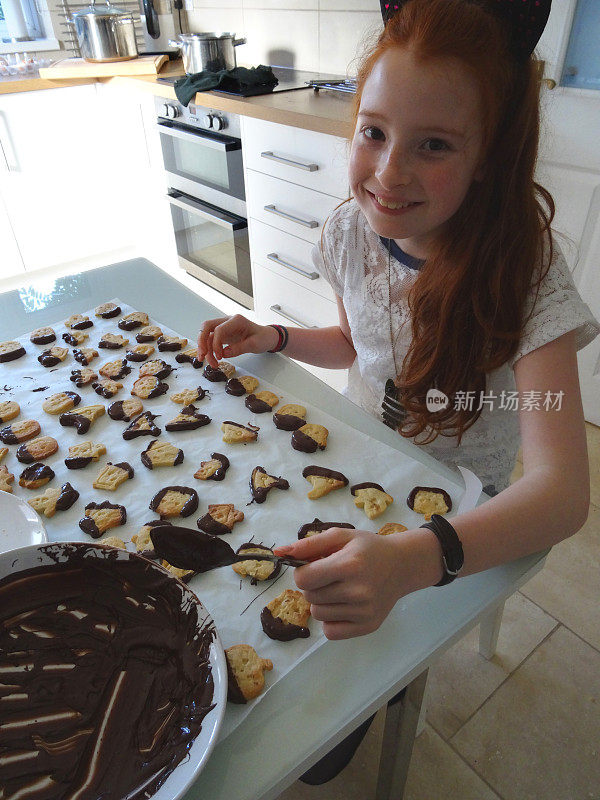 一个小女孩在做万圣节饼干，上面涂着巧克力糖霜