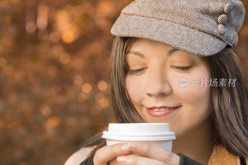 饮品:年轻女子在秋叶中捧着温暖的咖啡。