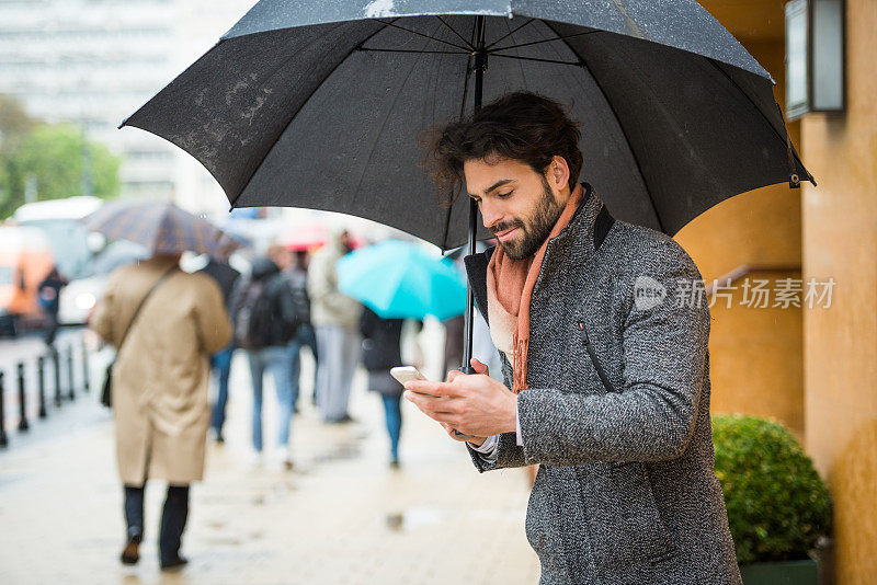 街上的男人拿着手机和雨伞