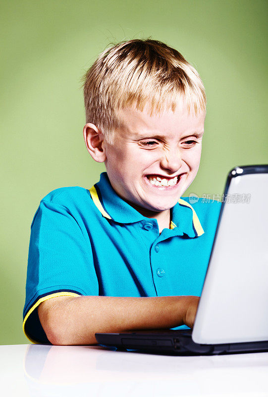 快乐的小男孩在用笔记本电脑时咧着嘴笑