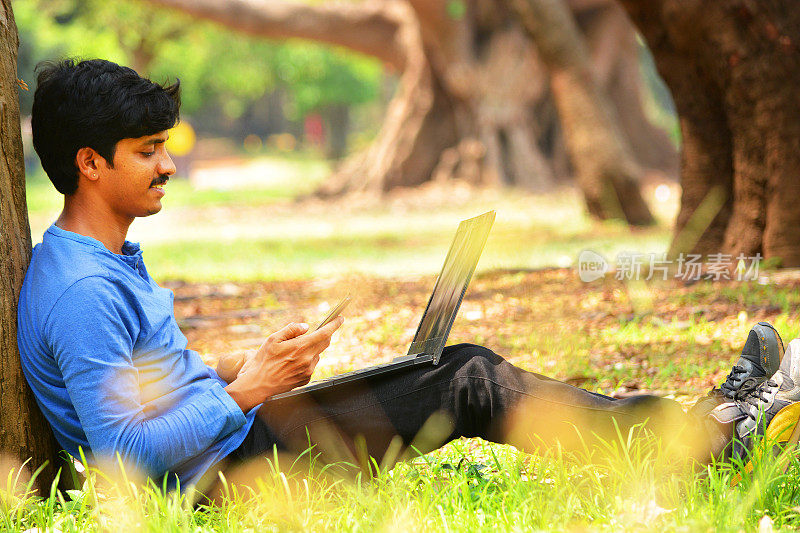 年轻的印度男子在公园里使用智能手机