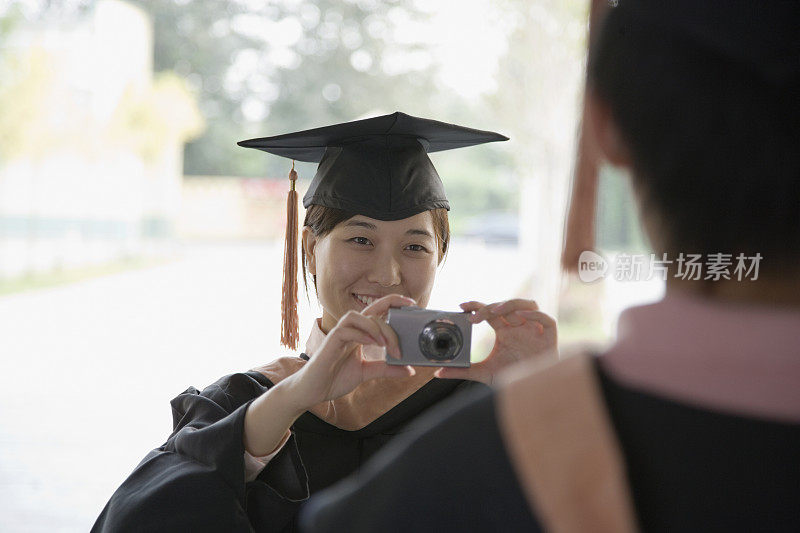 年轻女子在拍照的朋友在毕业礼服