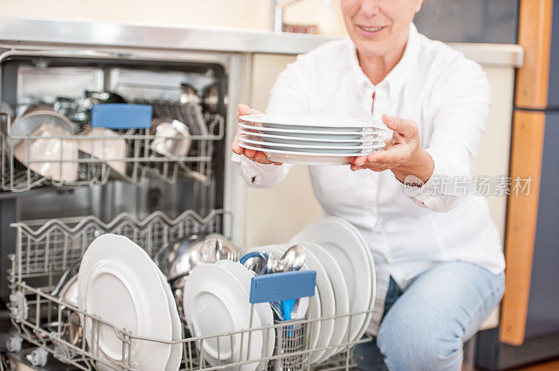 微笑的成年妇女正在卸载洗碗机