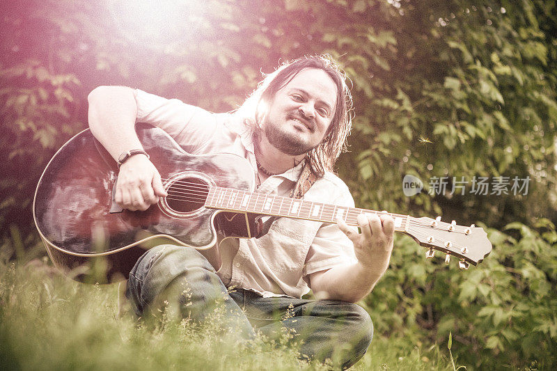 阳光下的男人在树林里弹普通的吉他