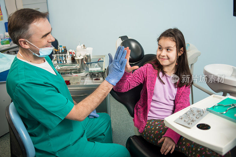 资深儿科牙医和可爱的孩子在牙科诊所治疗牙齿后，微笑着击掌。牙科、医学、口腔科和保健概念。牙科设备