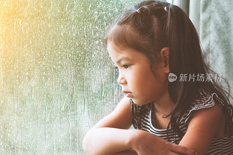 悲伤的亚洲小女孩望着窗外在雨天