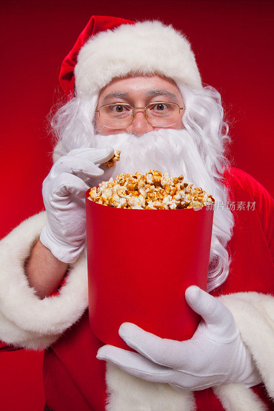 传统圣诞老人看电视，吃爆米花。圣诞节。红色的背景。的情绪。恐惧。惊喜